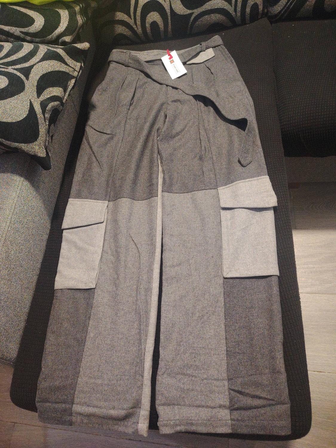 Grey trousers with large pockets on a sofa with black and white designer cushions. White label visible on the waistband.