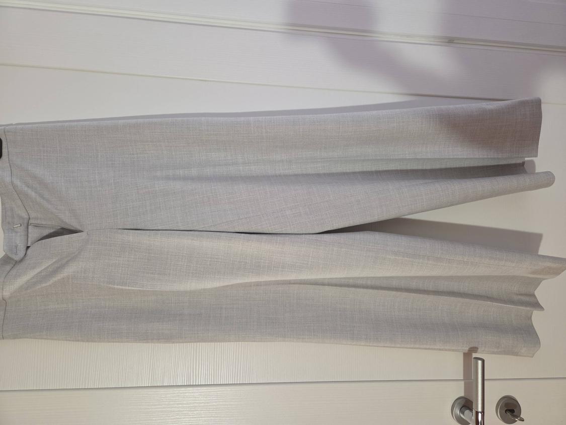 Light grey fabric trousers hanging on a white door, showcasing a wide-leg design and fluid drape.
