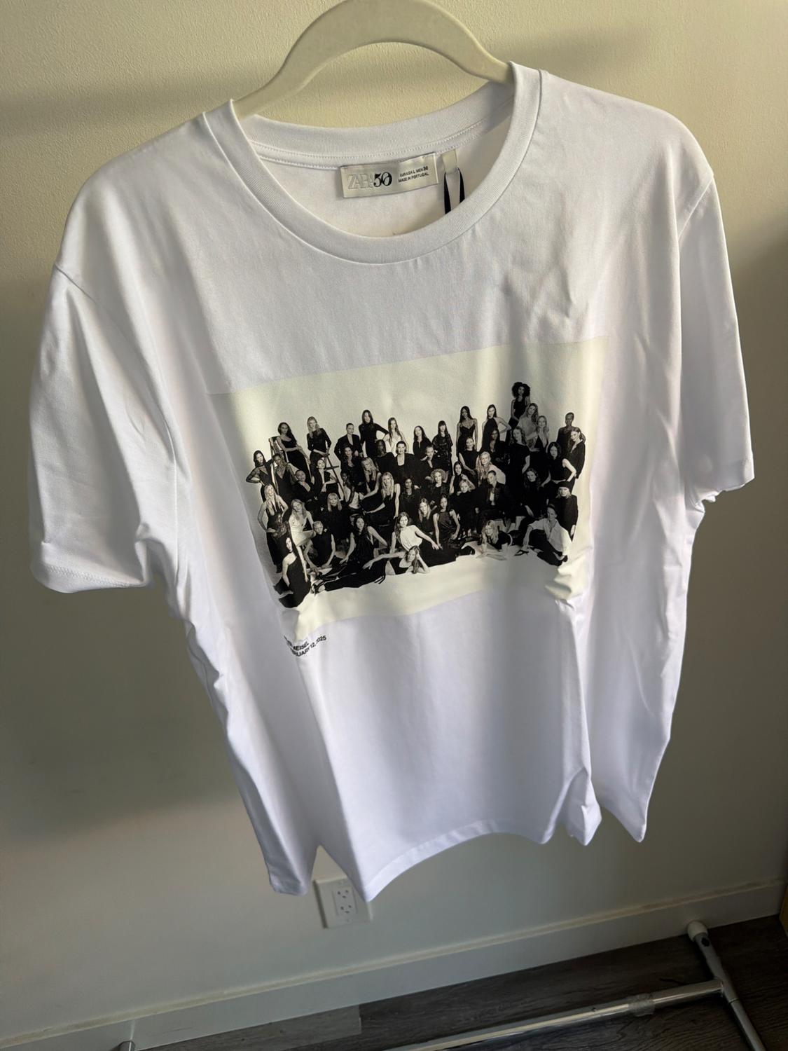 White t-shirt hanging with a black and white image of a group of people. Visible tag with "Zara 50".