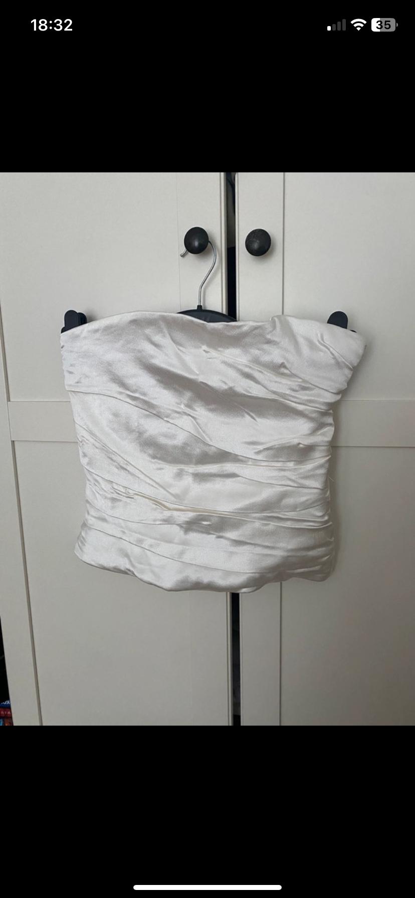 White satin top hanging on a black coat hanger in front of a white wardrobe with black knobs.