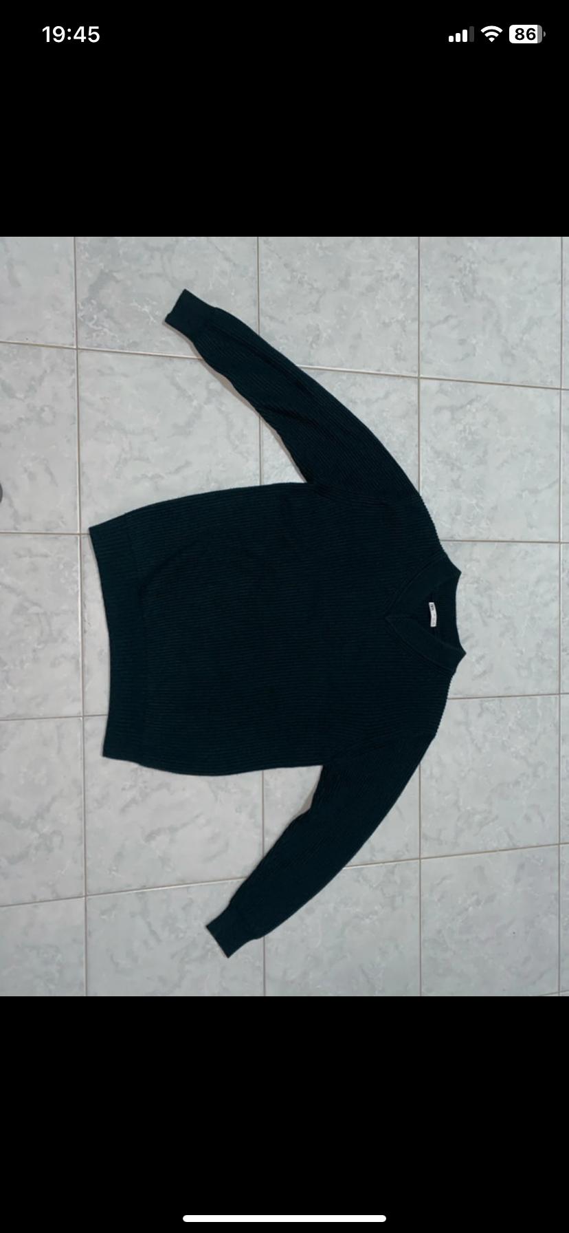 Black long-sleeved sweater on a white tiled floor. The label is visible on the neck. Time on screen: 19:45.