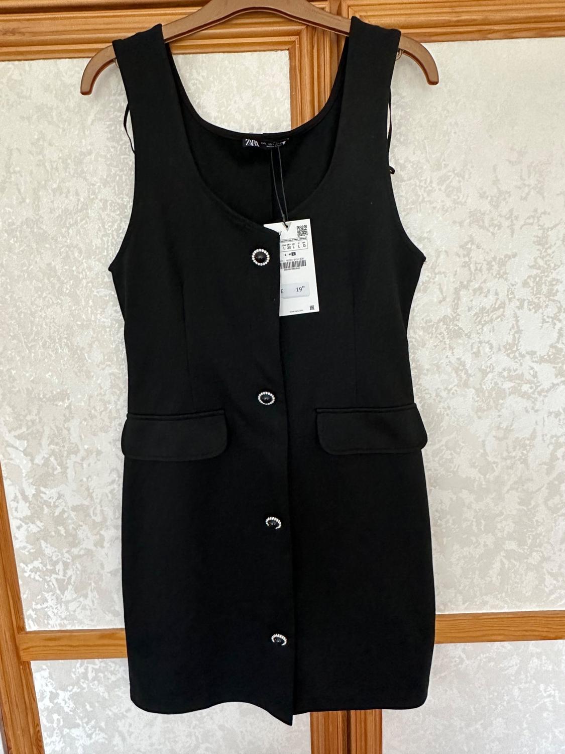 Front view of black dress with decorative buttons and front flap pockets.