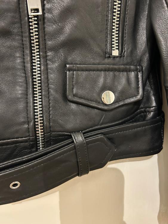 Detail of a black leather jacket with metallic zips and a flap pocket with a silver button.