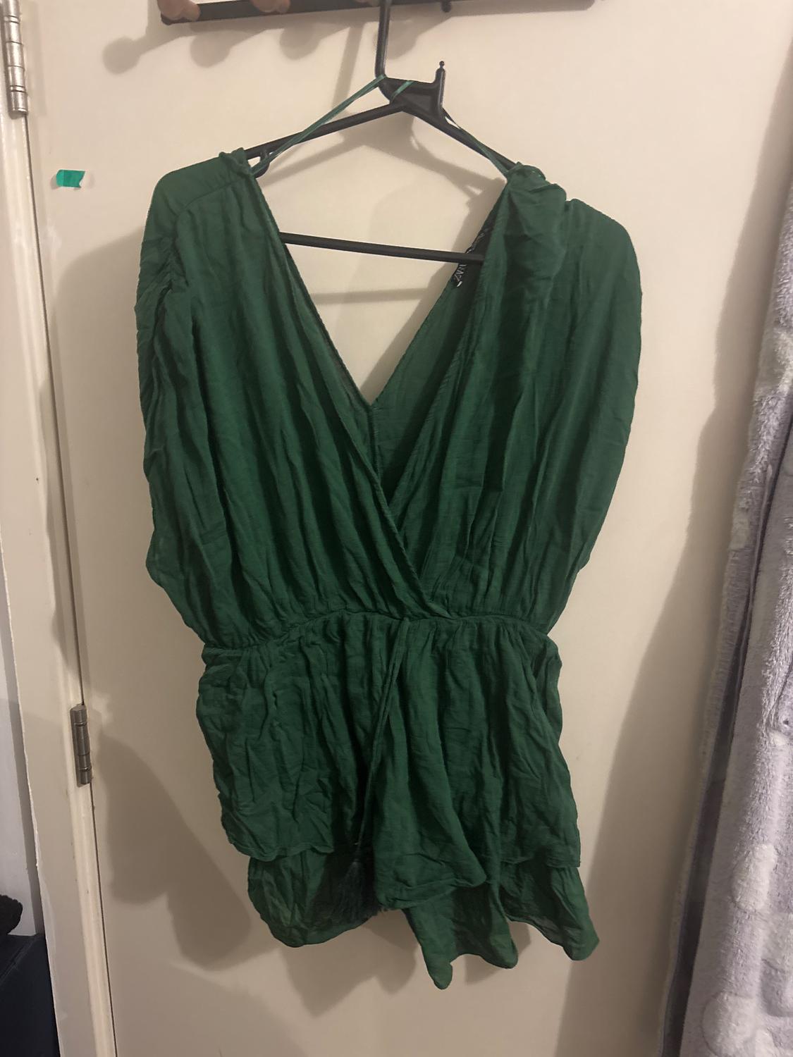 Green dress hanging on a black hanger over a white door. Wrinkled fabric and V-neck design.