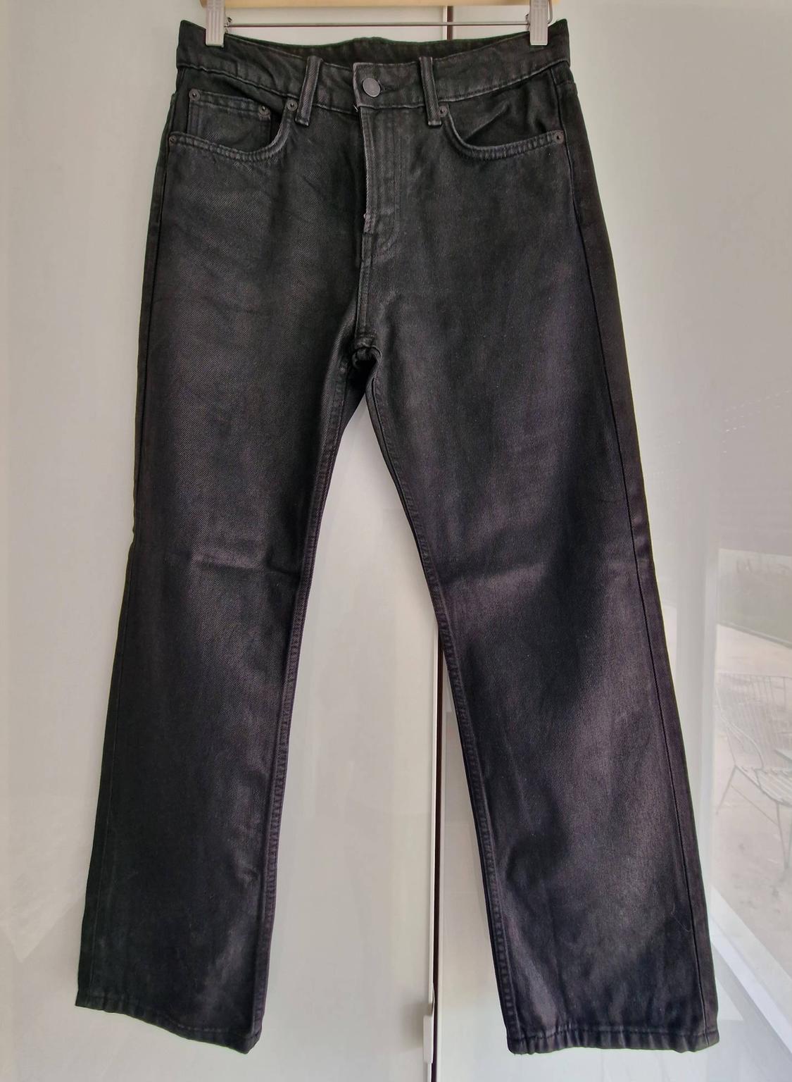 Black denim jeans hanging on a hanger against a white background. Five-pocket design with front button fastening.