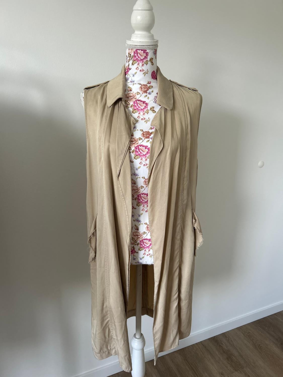 Mannequin with a sleeveless beige gilet against a white background, with a pink and white floral pattern on the mannequin's torso.