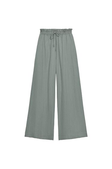 Front view of sand-coloured flowy trousers, elasticated drawstring waist and concealed side pockets, wide leg.