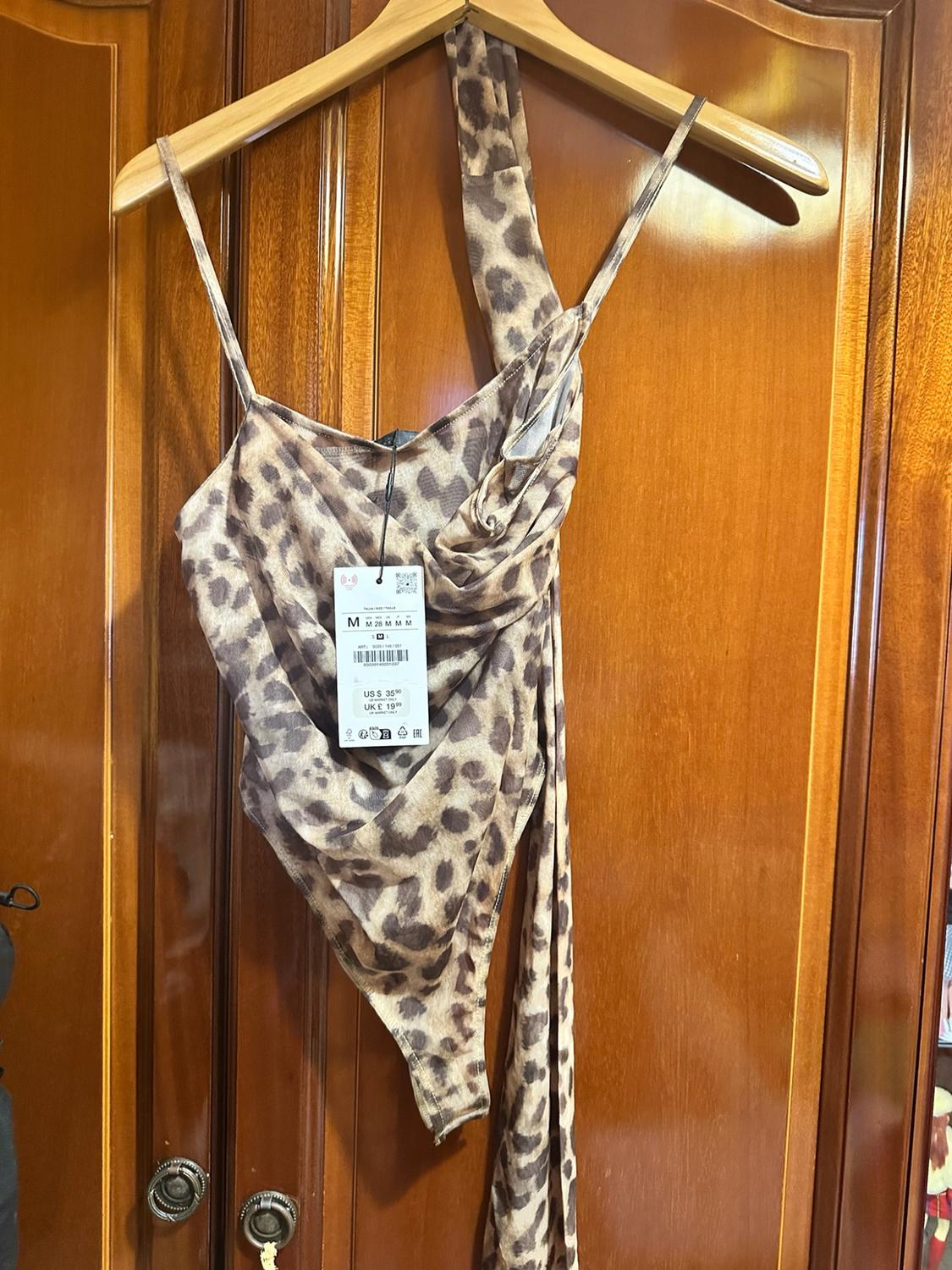Asymmetric leopard-print bodysuit on a hanger over a wooden door. Text: M M 28 M M M US $ 35.90 UK £ 19.99.
