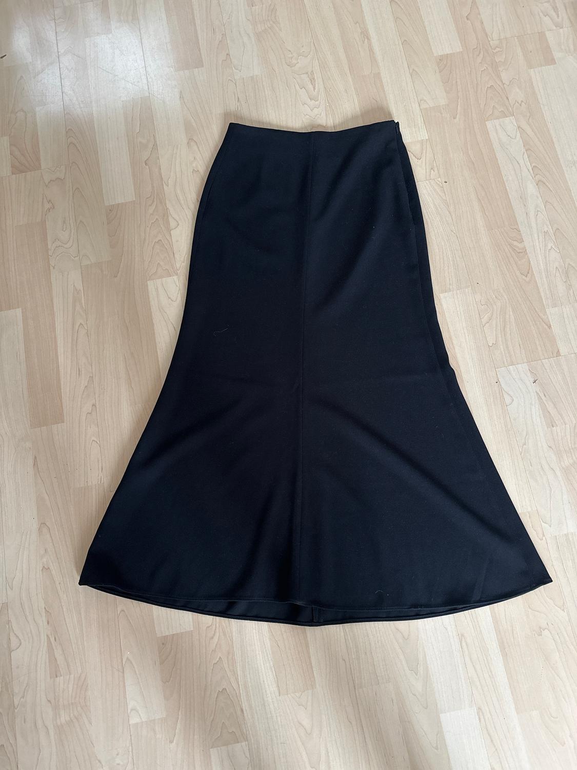 Long black flared skirt on a light wooden floor.