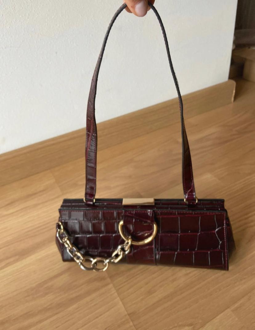 Side view of a dark brown handbag with a crocodile texture and a decorative gold chain.