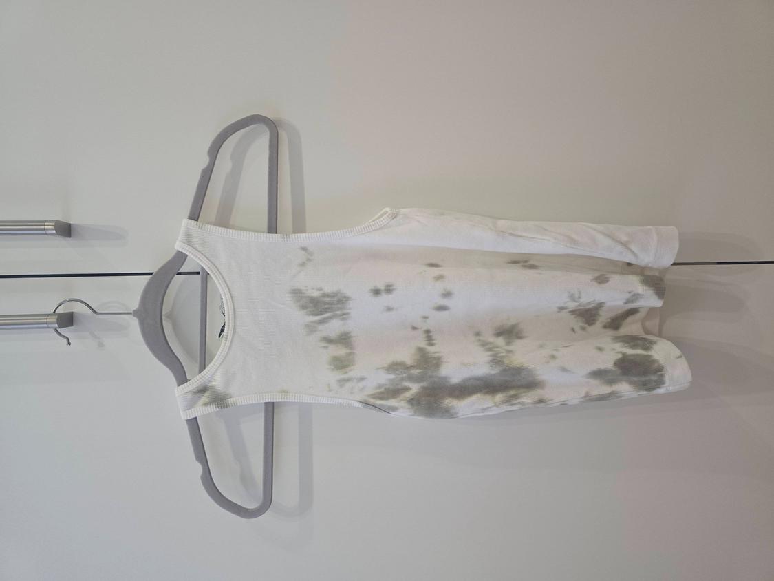 Λευκό αμάνικο μπλουζάκι με γκρι στάμπα tie-dye, κρεμασμένο σε μια γκρι κρεμάστρα πάνω σε λευκό φόντο.
