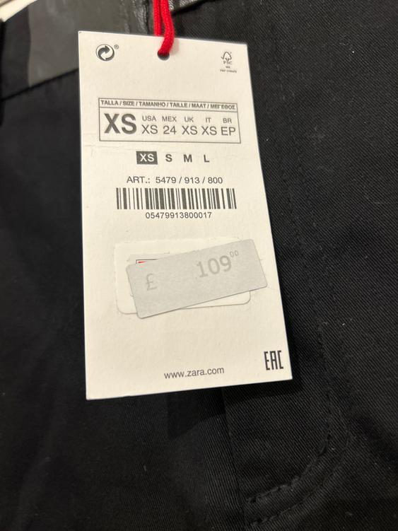 Clothing label with sizes XS, S, M, L and price of £109.00. Includes barcode and website www.zara.com. Black background.