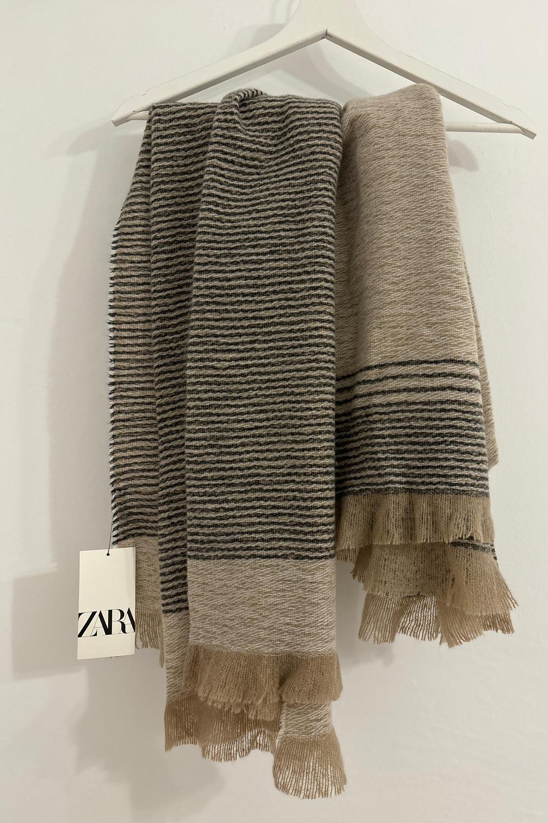Beige and black striped scarf with fringes hanging on a hanger.