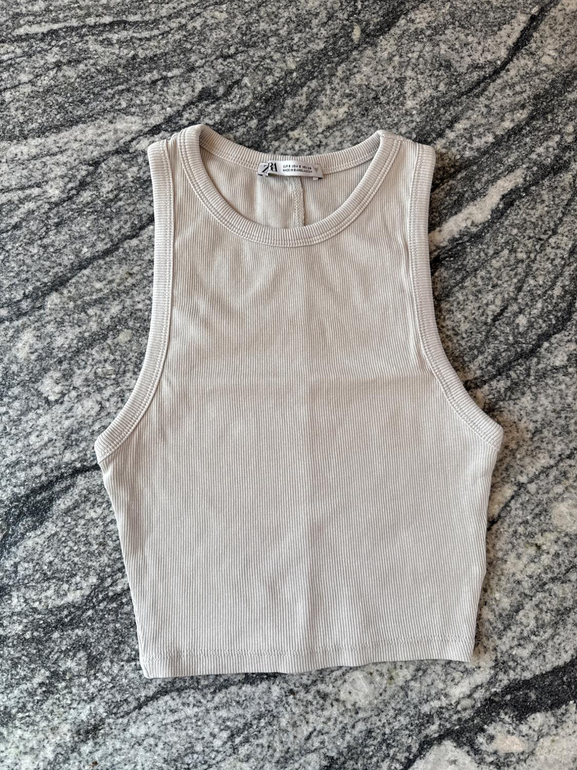 Beige sleeveless top on a grey marble background. Label visible on the neck with text: "ZARA".