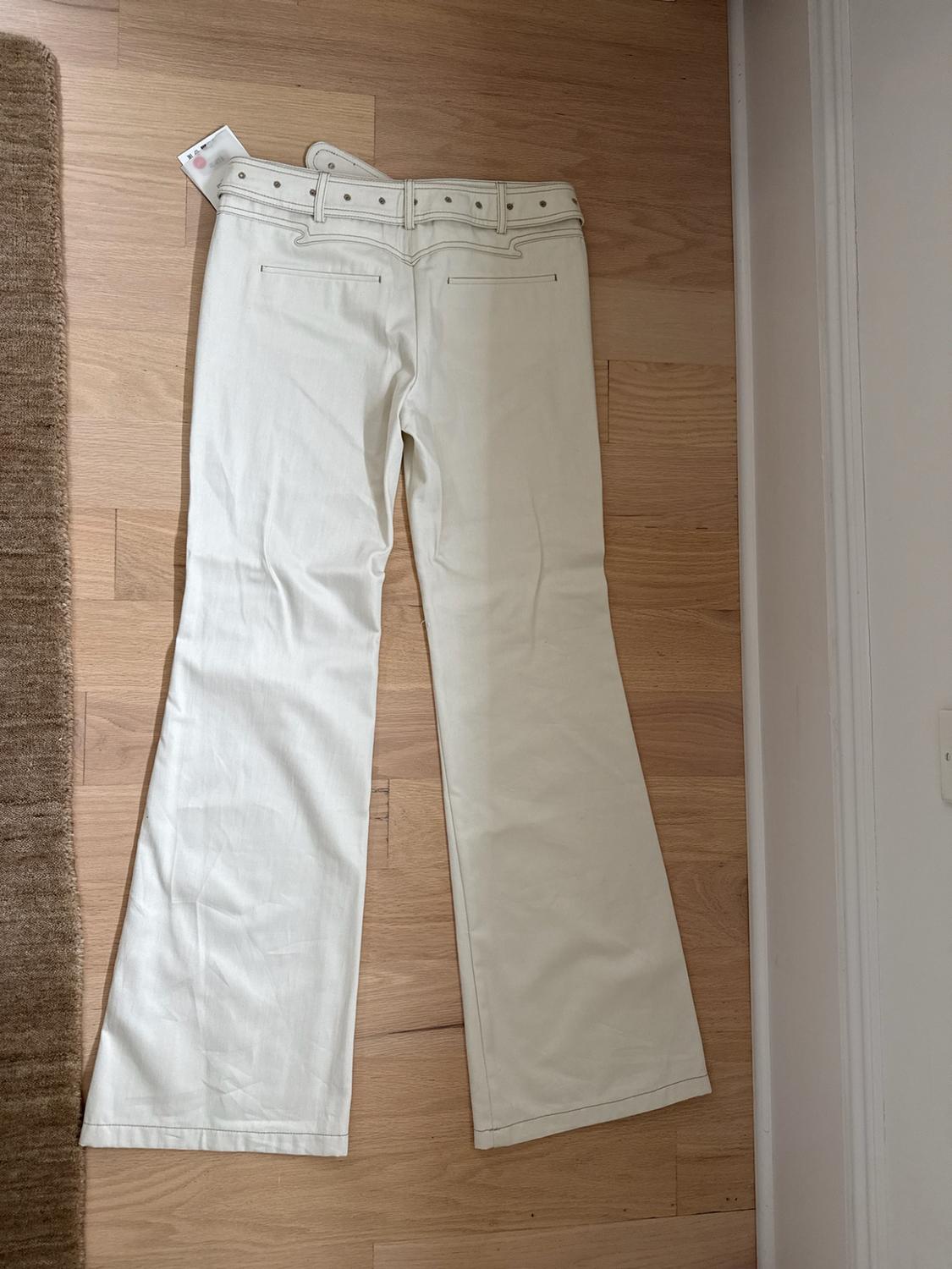White flared pants with a belt, seen from behind. Laid out on a light wood floor next to a rug in a casual setting.