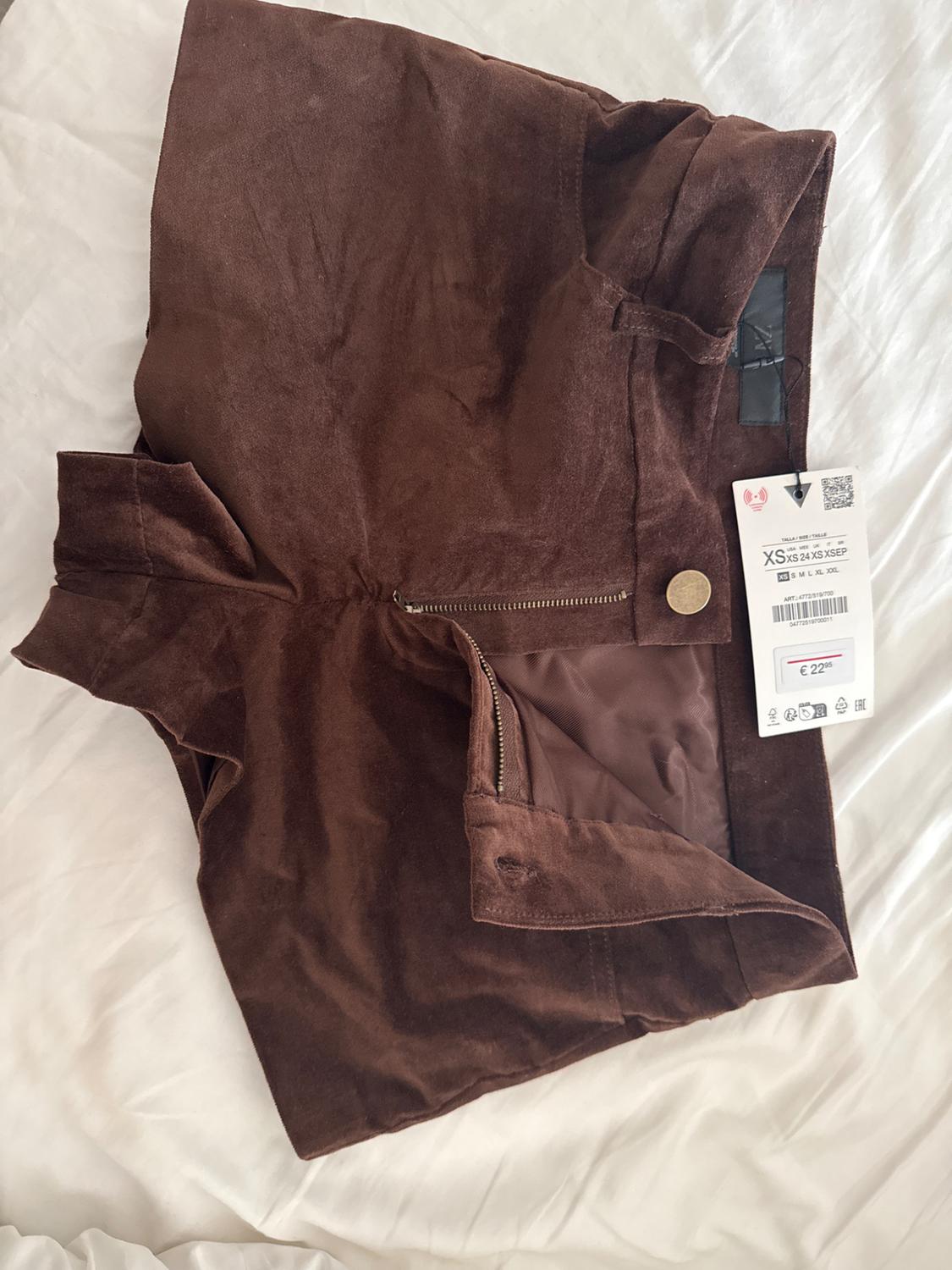 Brown velvet shorts with a zip and gold button, visible price tag of €22.95 on a white bed.