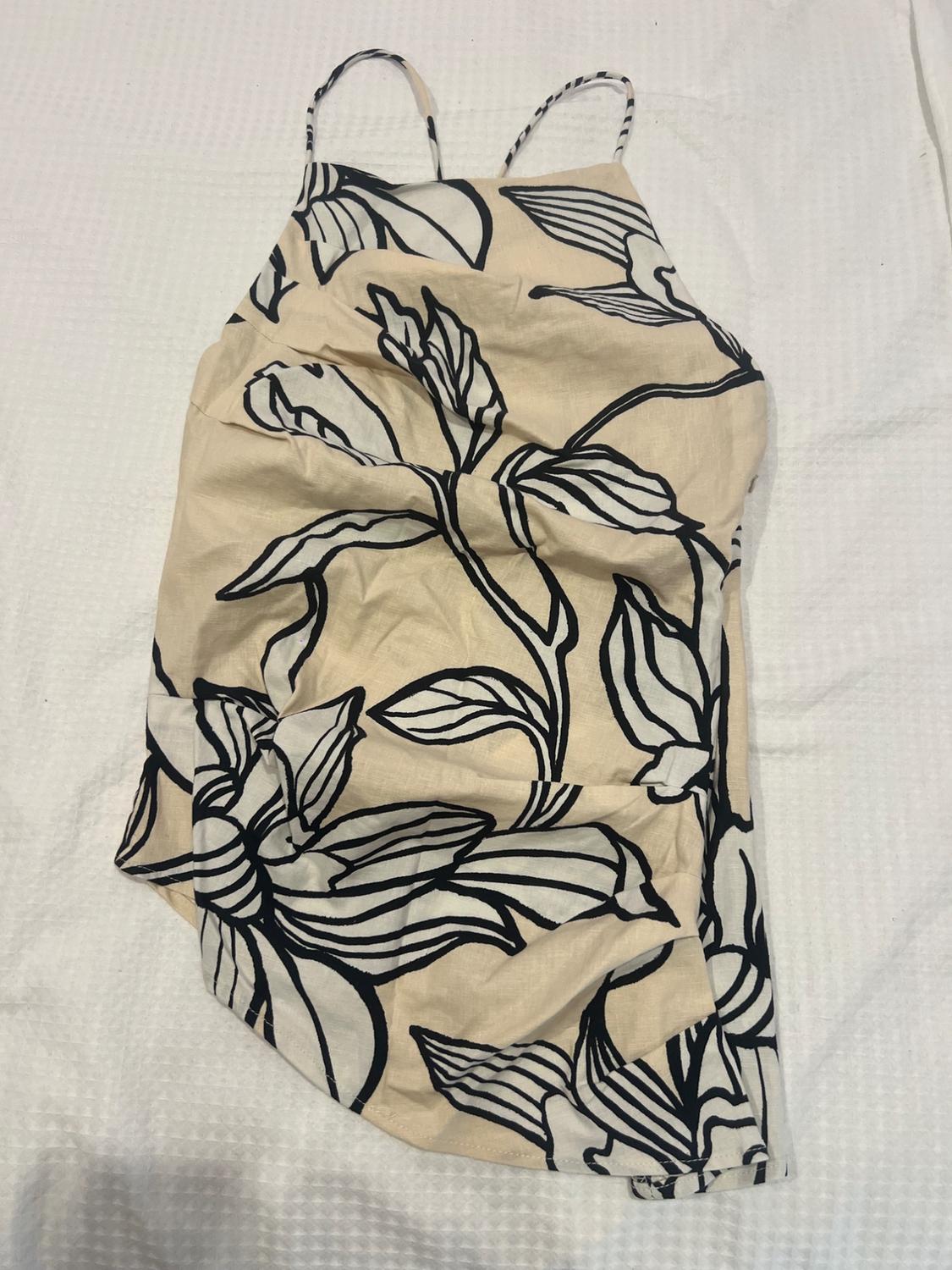 Beige garment with thin straps and a black floral print, on a textured white surface.