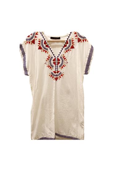 Front view of a white blouse with red and blue geometric embroidery on the chest and short sleeves.