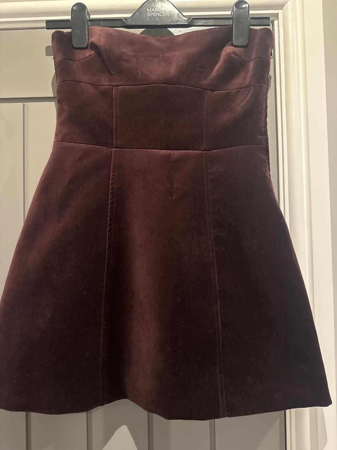 Dark brown velvet skirt hanging on a black "Marks & Spencer" hanger over a beige door.