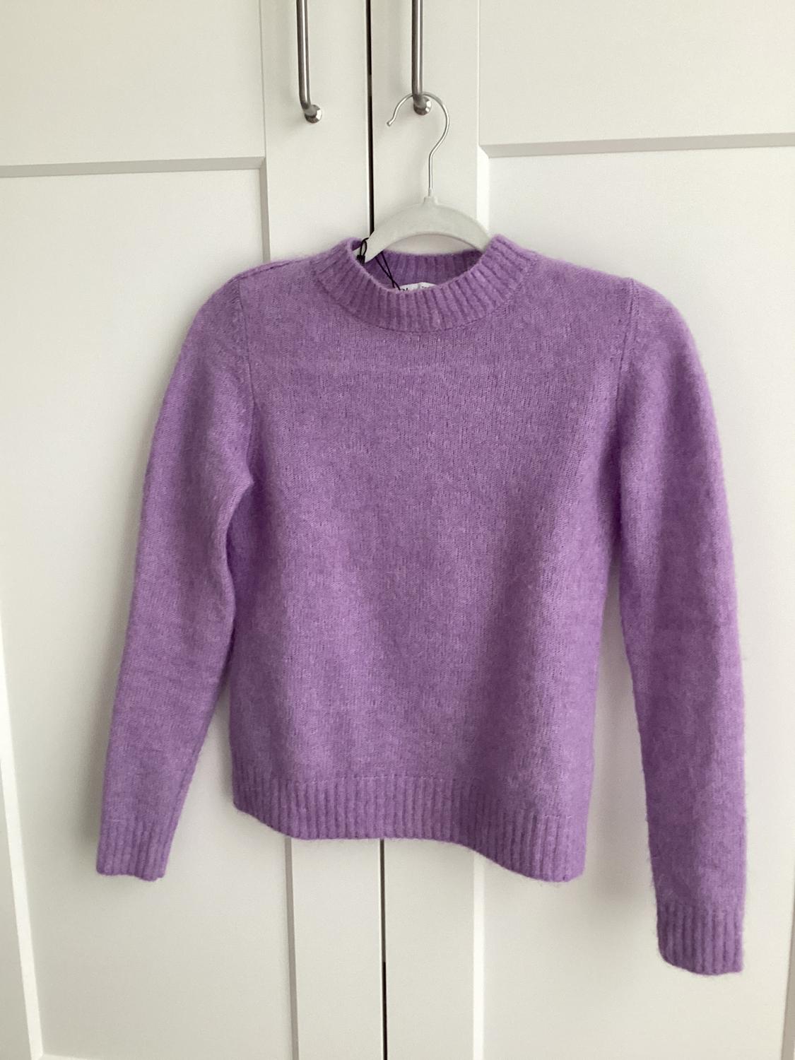 Lilac knitted jumper hanging on a hanger in front of a white wardrobe with panelled doors and metal handles.