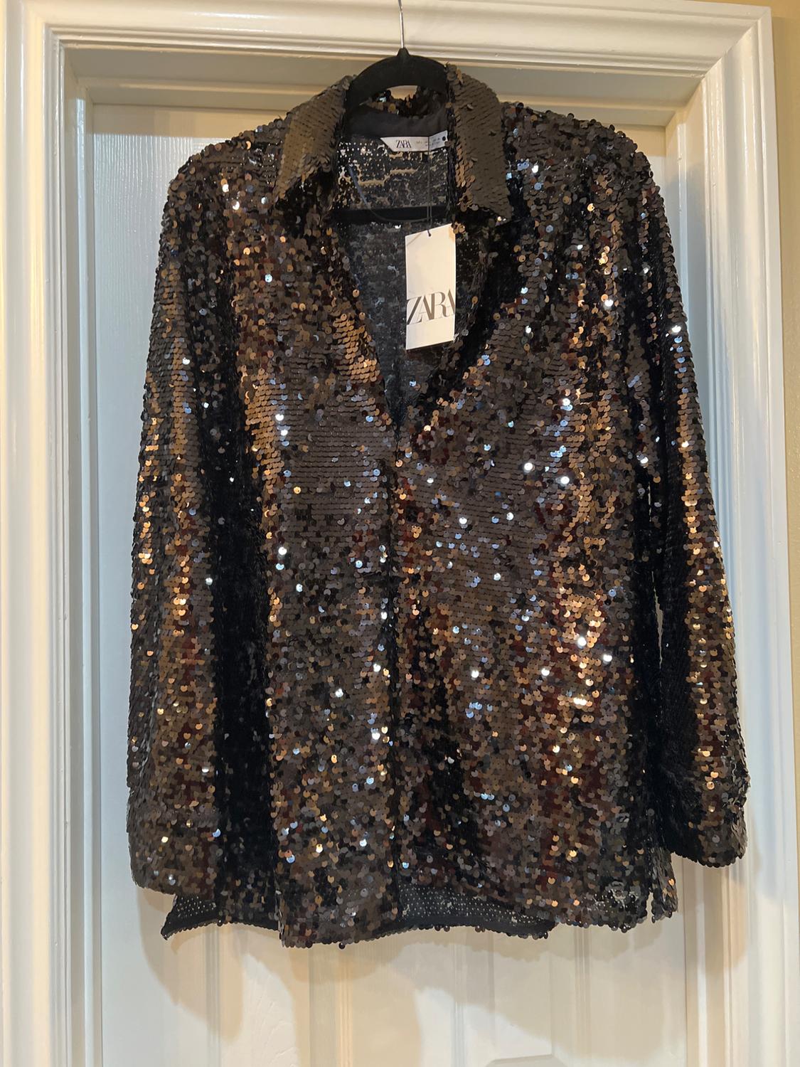 Black sequin shirt hanging on a white door. Visible label with the text "ZARA".