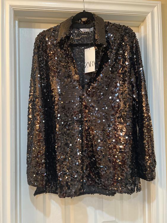 Black sequin shirt hanging on a white door. Visible tag with the text "ZARA".