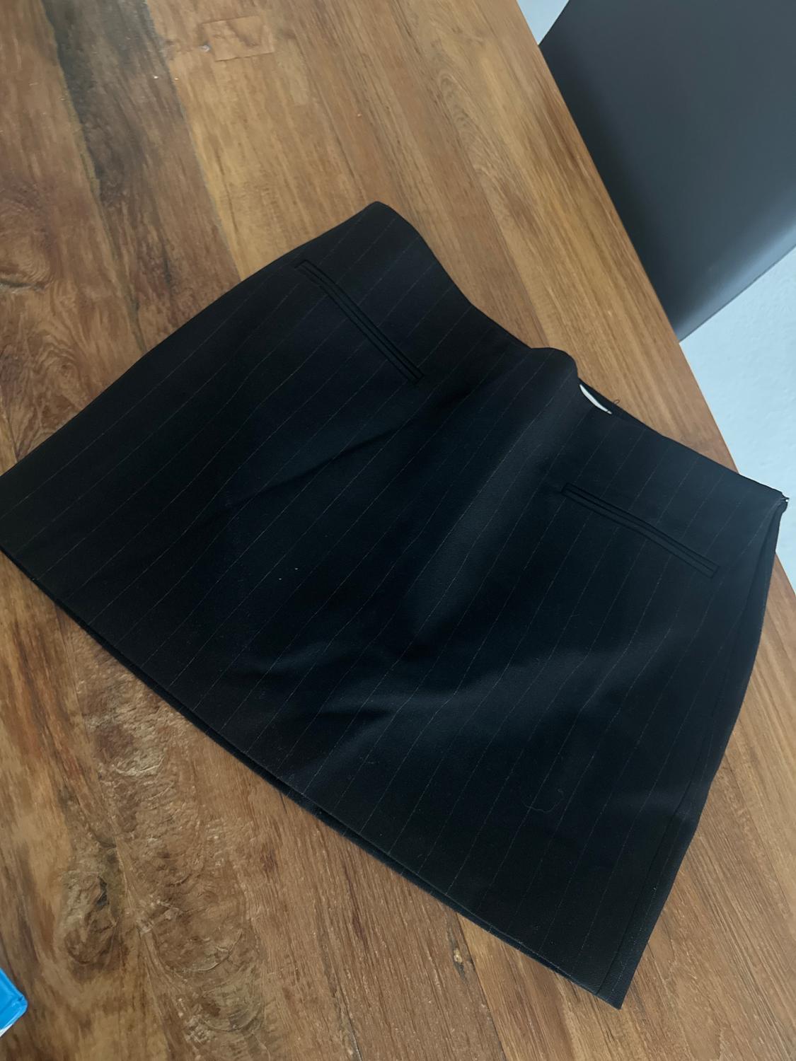 Black pinstriped skirt on a wooden table. The skirt has two back pockets and a simple, elegant design.