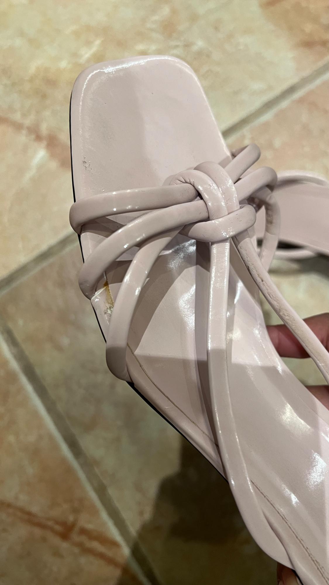 Light beige low-heeled sandal with interwoven straps, on a brown-toned tiled floor.
