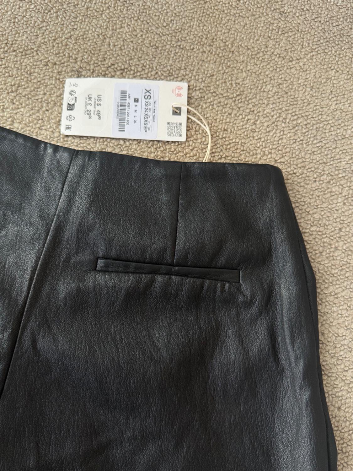 Black garment with pocket on a carpet. Label: SIZE XS 24 XS XS EP ART: 4387/295/800 US $49.90 UK £29.99.