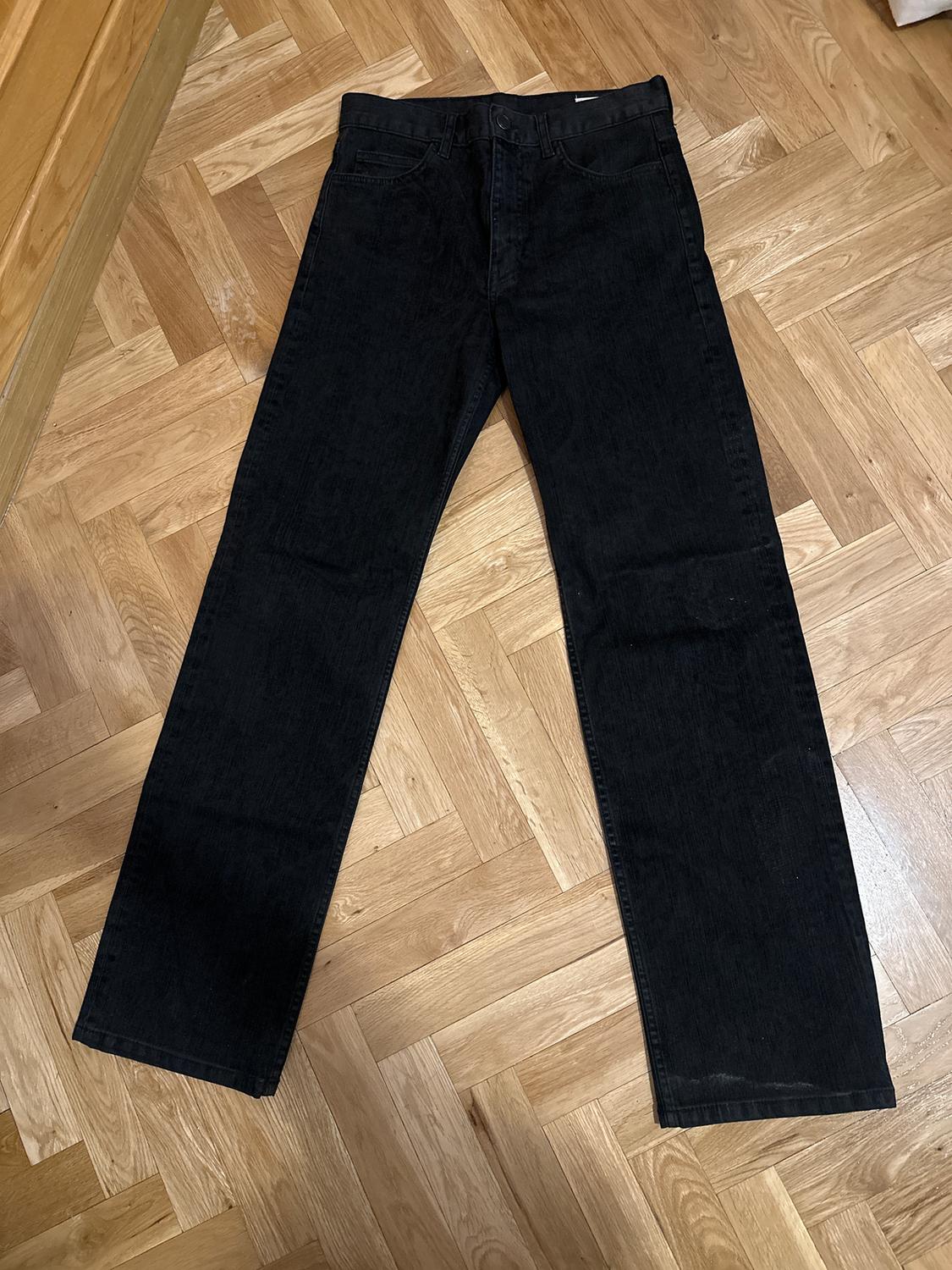 Black straight-leg jeans laid out on a light wooden parquet floor.