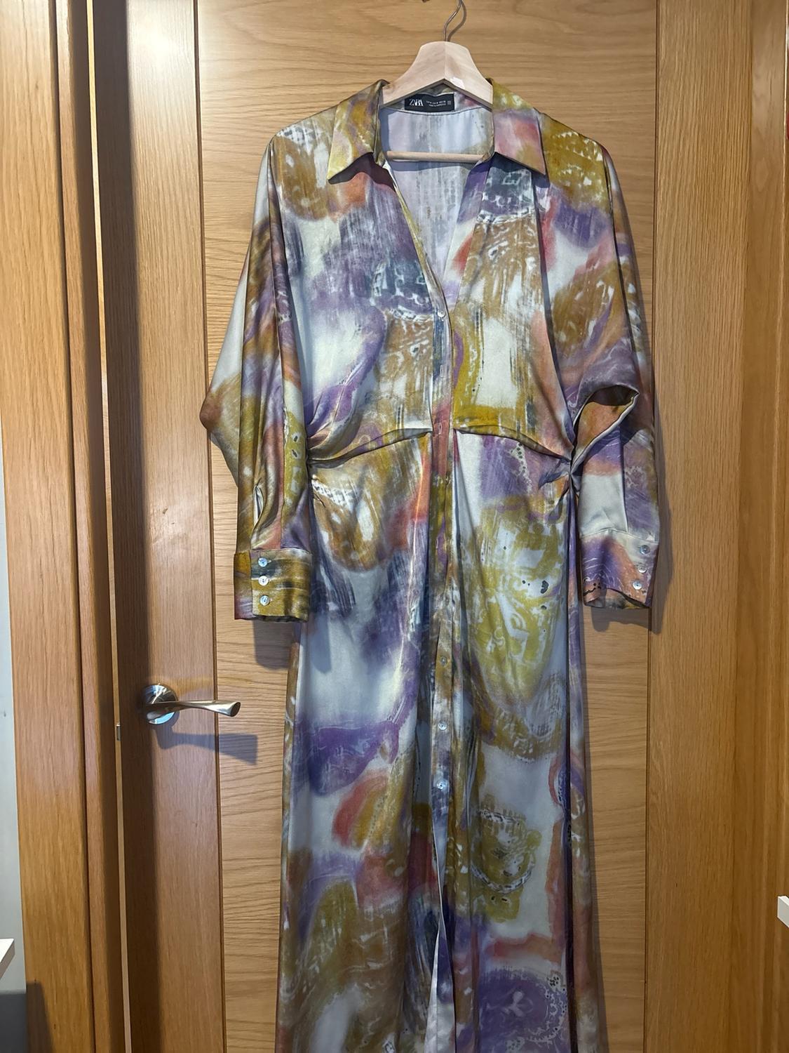 Long shirt dress with an abstract purple, yellow and white print, hanging on a wooden door. Text ZARA.