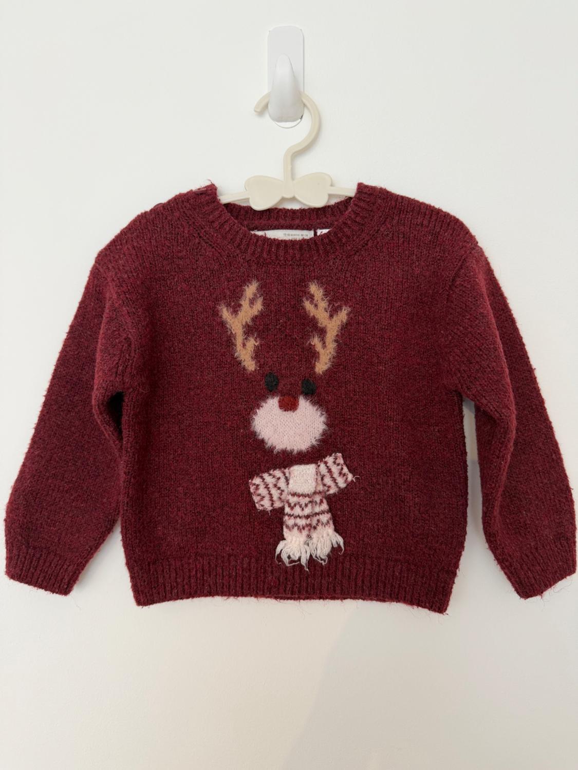 Maroon knitted jumper with a red-nosed reindeer and scarf. Hanging on a white coat hanger against a white background. Festive and cosy style.