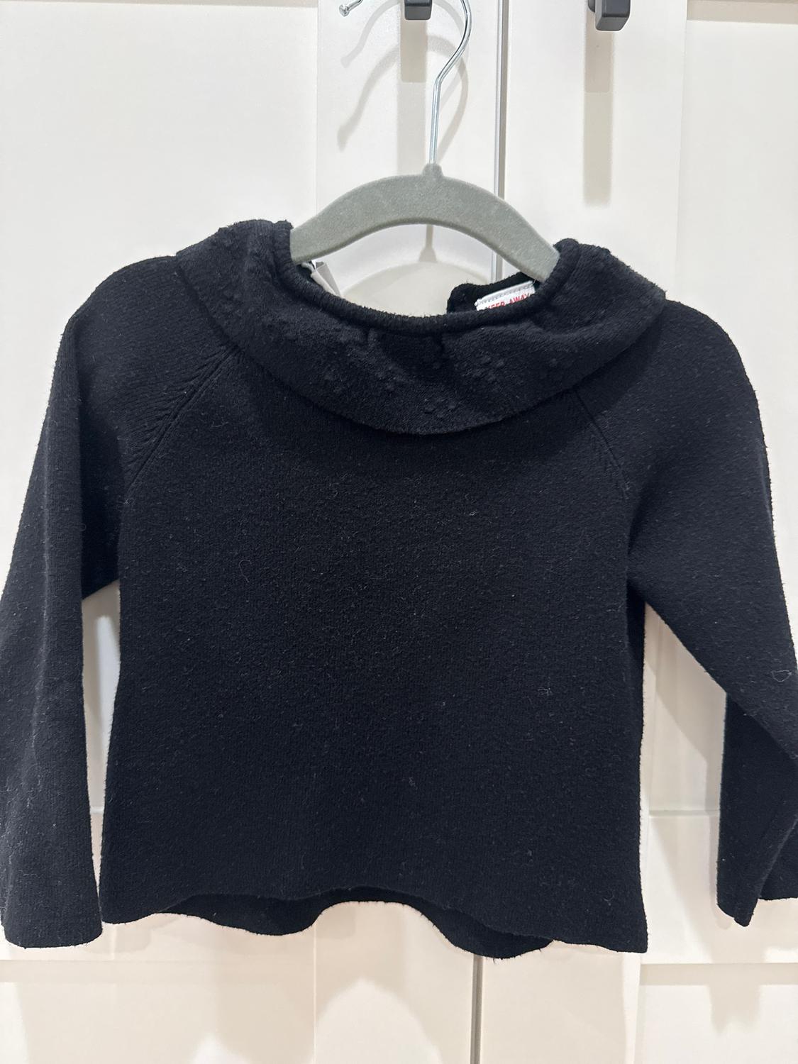 Black long-sleeved jumper hanging on a grey hanger against a white background.
