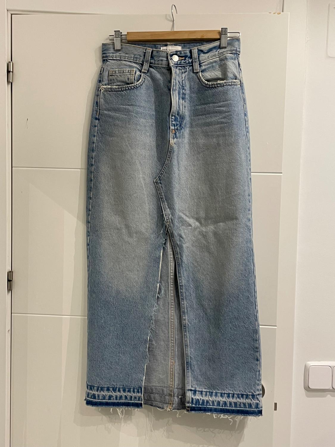 Light blue denim maxi skirt with a front slit, hanging on a wooden hanger over a white door.