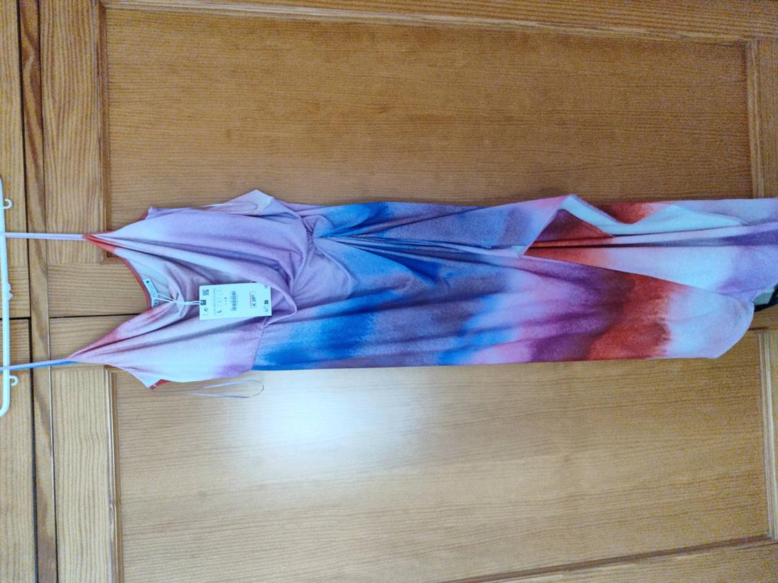 Long dress with a faded print in shades of pink, blue, and red, hanging on a white hanger in front of a wooden door.