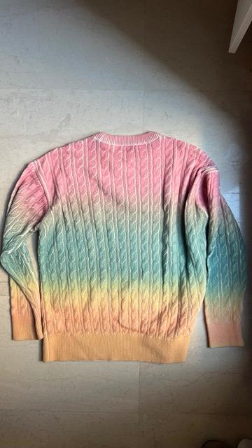 Knitted jumper with a gradient design in shades of pink, blue and yellow, against a light floor background.