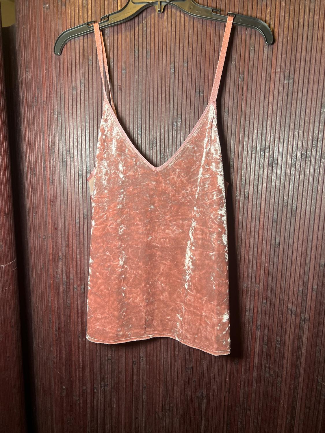 Pink velvet tank top hanging on a black hanger against a brown wooden background with vertical texture.