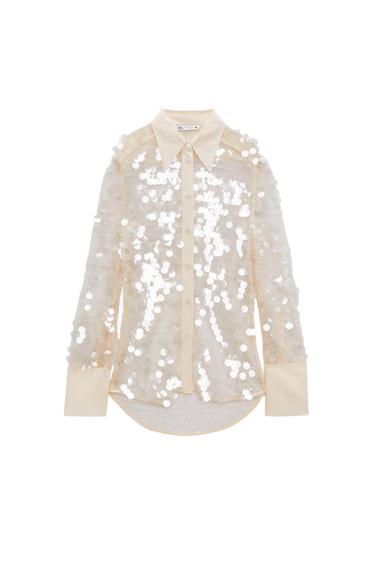 Beige shirt with large white sequins, classic collar, and wide cuffs. White background. Visible tag on the collar.