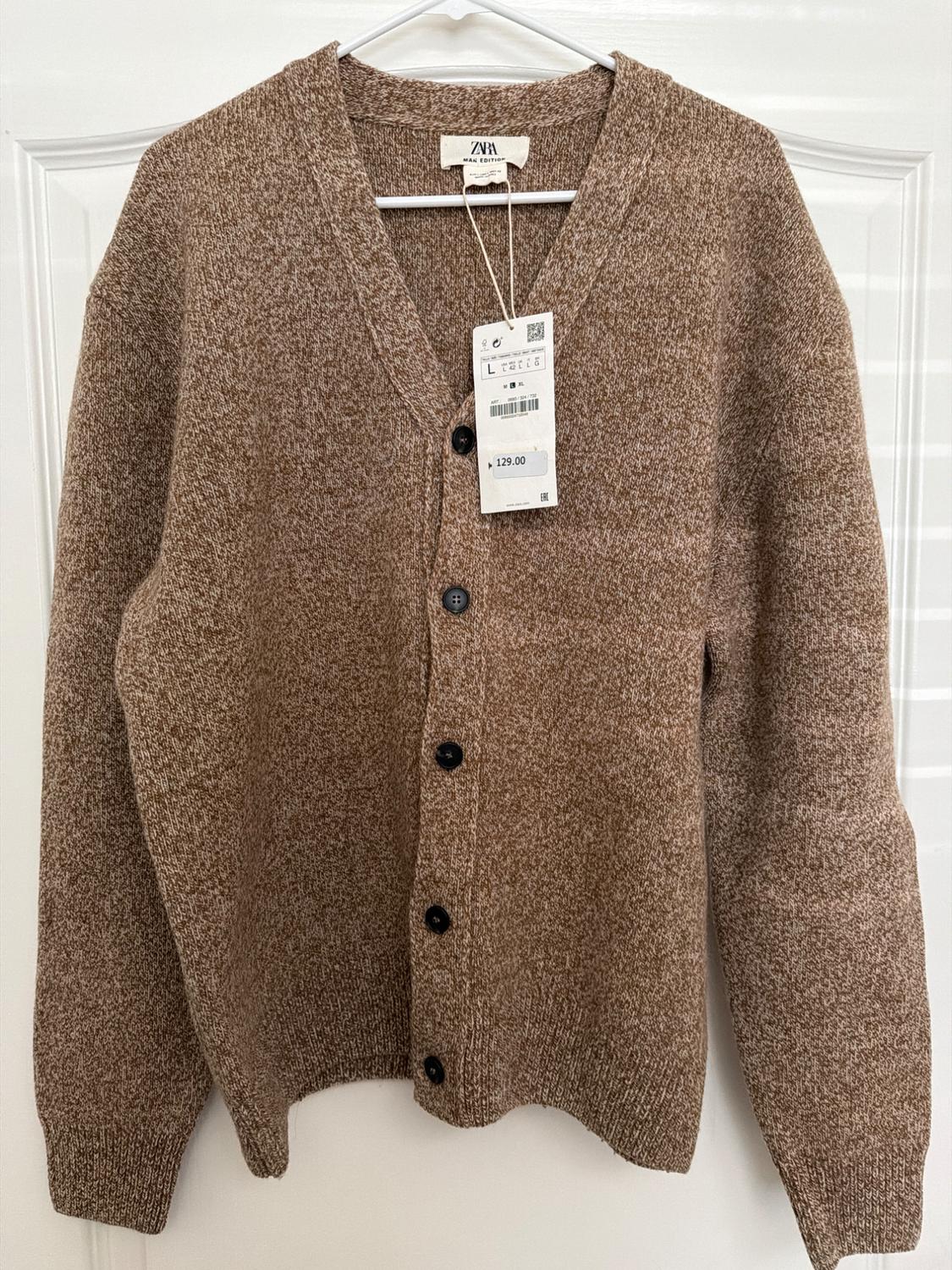Brown chunky knit cardigan with black buttons, hanging on a white hanger. Visible tag with price of 129.00.