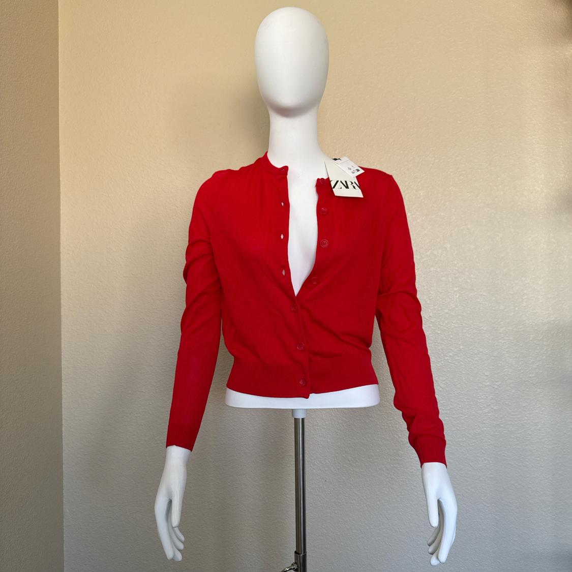 White mannequin with red buttoned cardigan, visible tag on shoulder. Plain beige background.