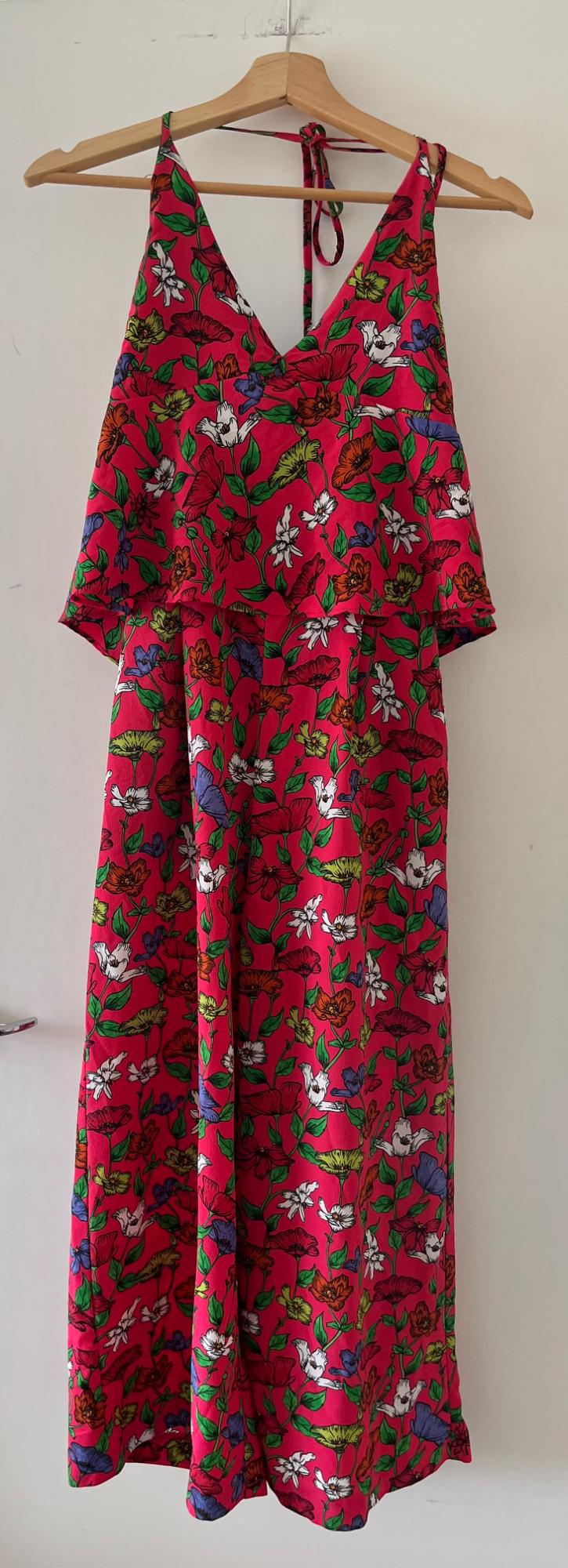 Fuchsia floral print halter-neck dress with frill, hanging on a wooden hanger on a white door. Casual and relaxed style.