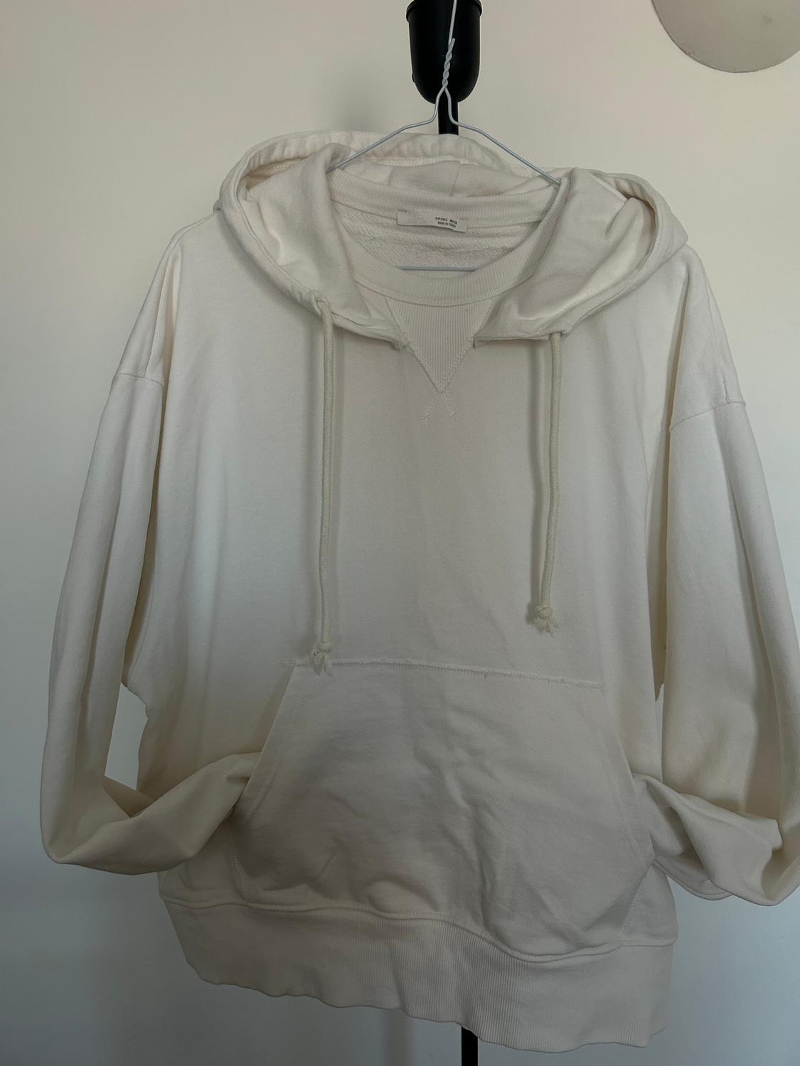 White hoodie with a drawstring, hanging on a black hanger against a white background.