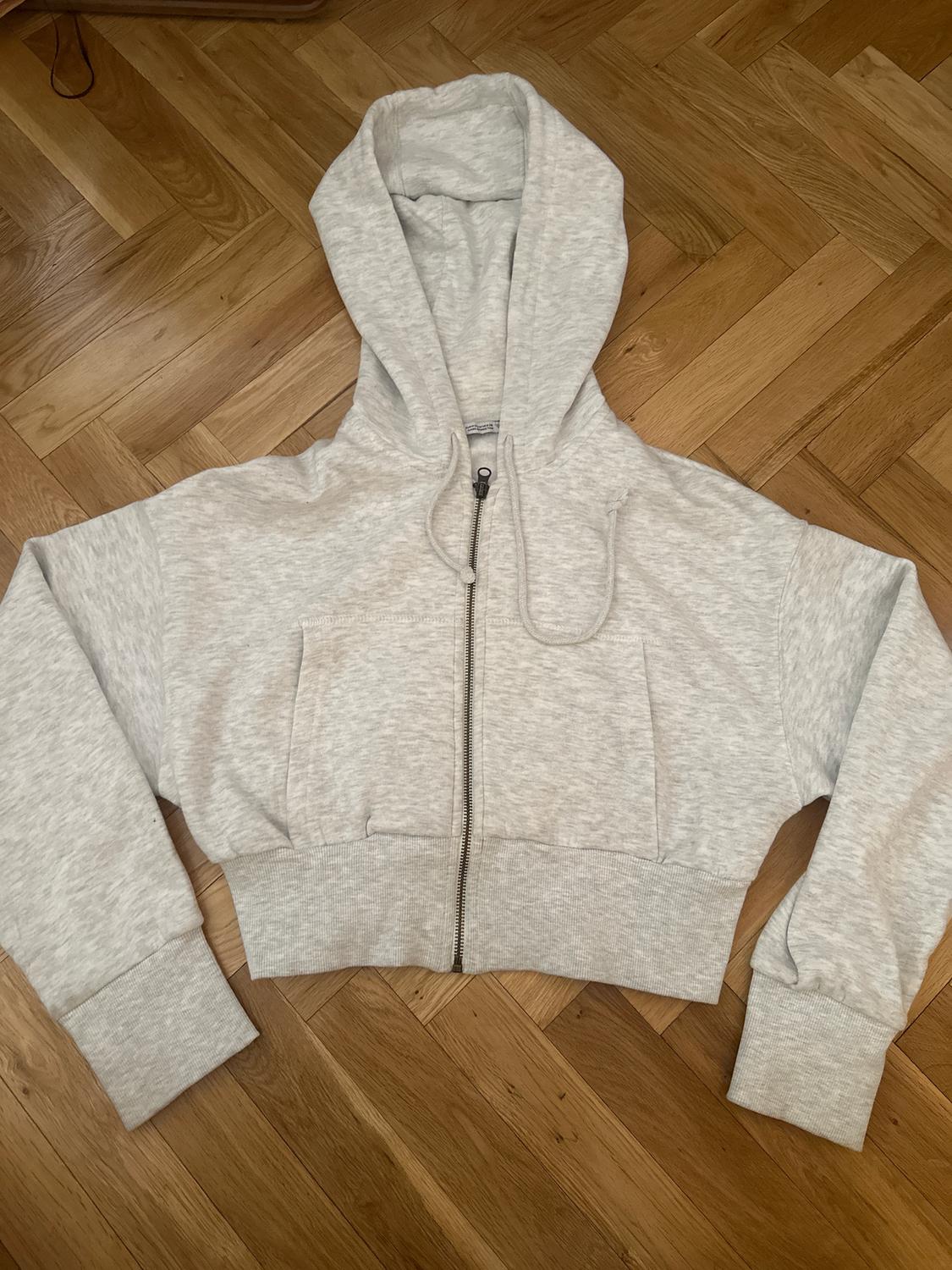 Grey hooded zip-up sweatshirt with long sleeves, on a light wooden floor.