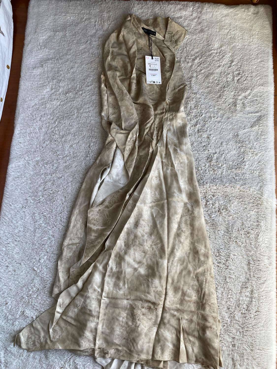 Long sleeveless dress in beige tones with a marbled pattern and split, laid out on a soft-textured carpet.