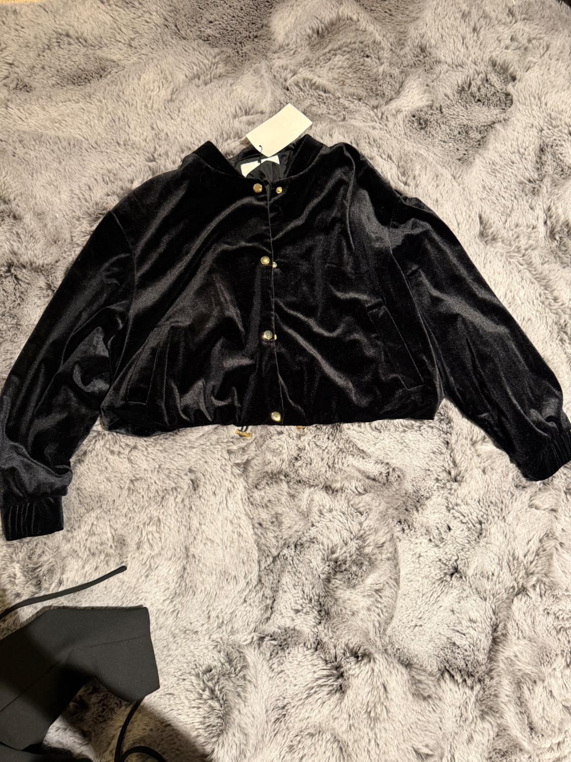 Black velvet jacket with gold buttons on a gray furry blanket. White tag visible on the collar.