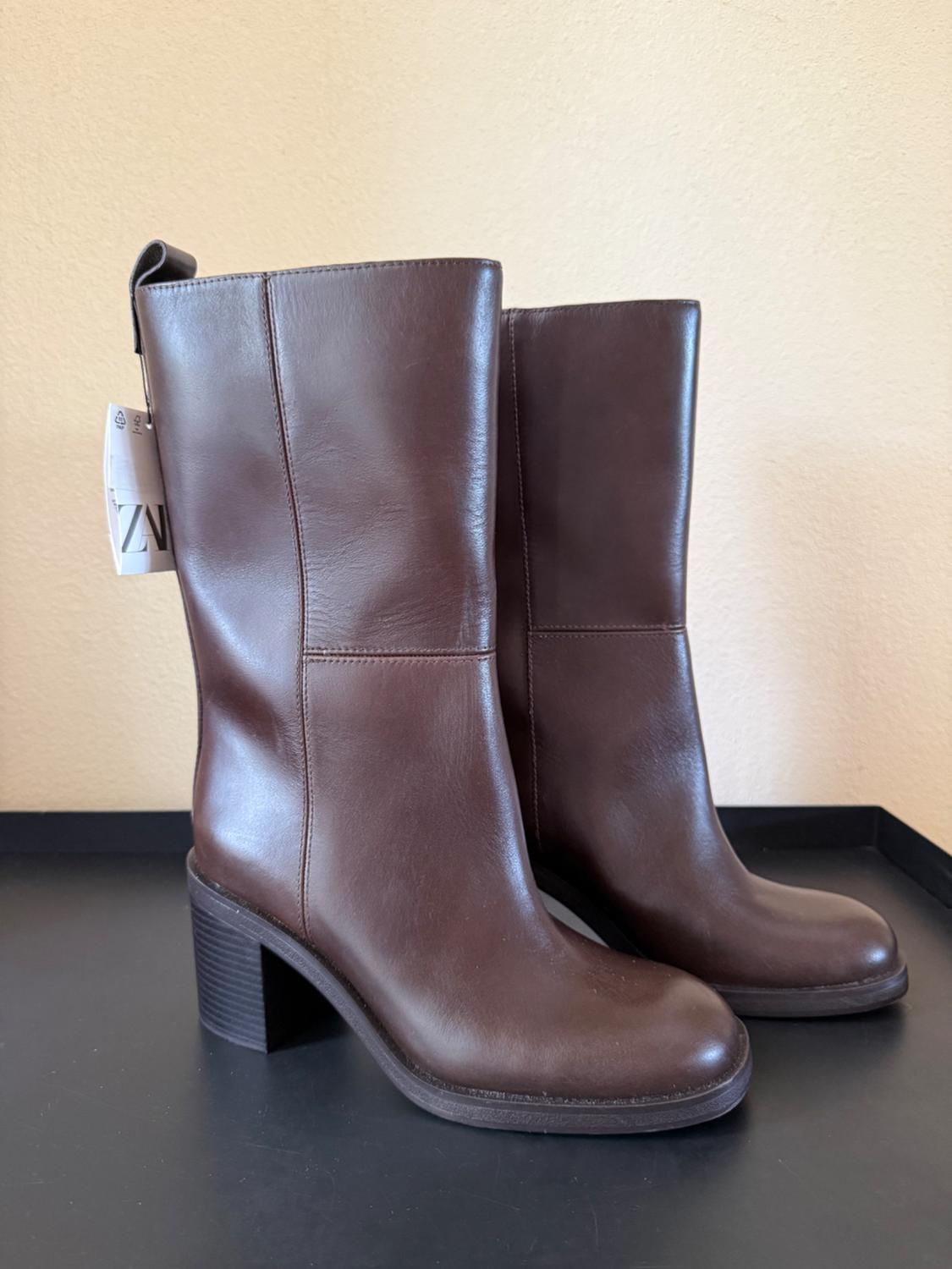 Brown leather boots with chunky heels on a black background. Visible tag in the upper left corner.
