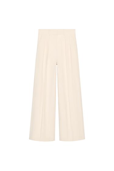 Front view of wide-leg cream-colored pants with pleats and side pockets.