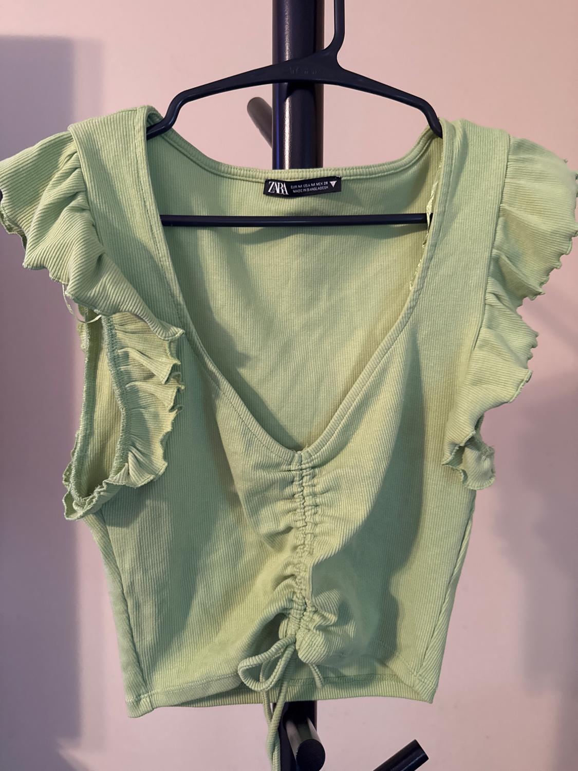 Front view of a green top with ruffled sleeves and adjustable ruching in the center.