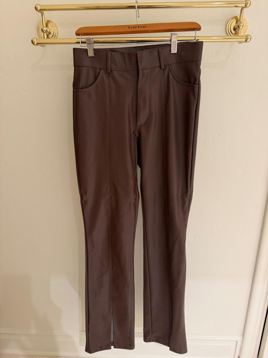 Brown trousers hanging on a wooden hanger with the brand "bebe" engraved, against a light background.