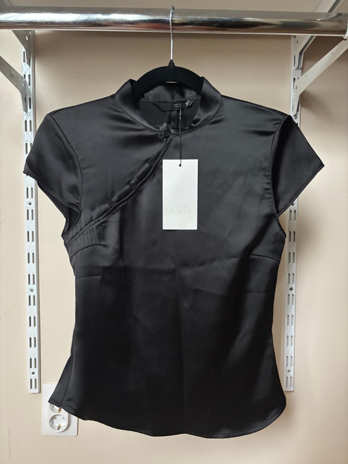 Short-sleeved satin black top with an asymmetric buttoned mandarin collar, on a hanger. Label with the text ZARA.